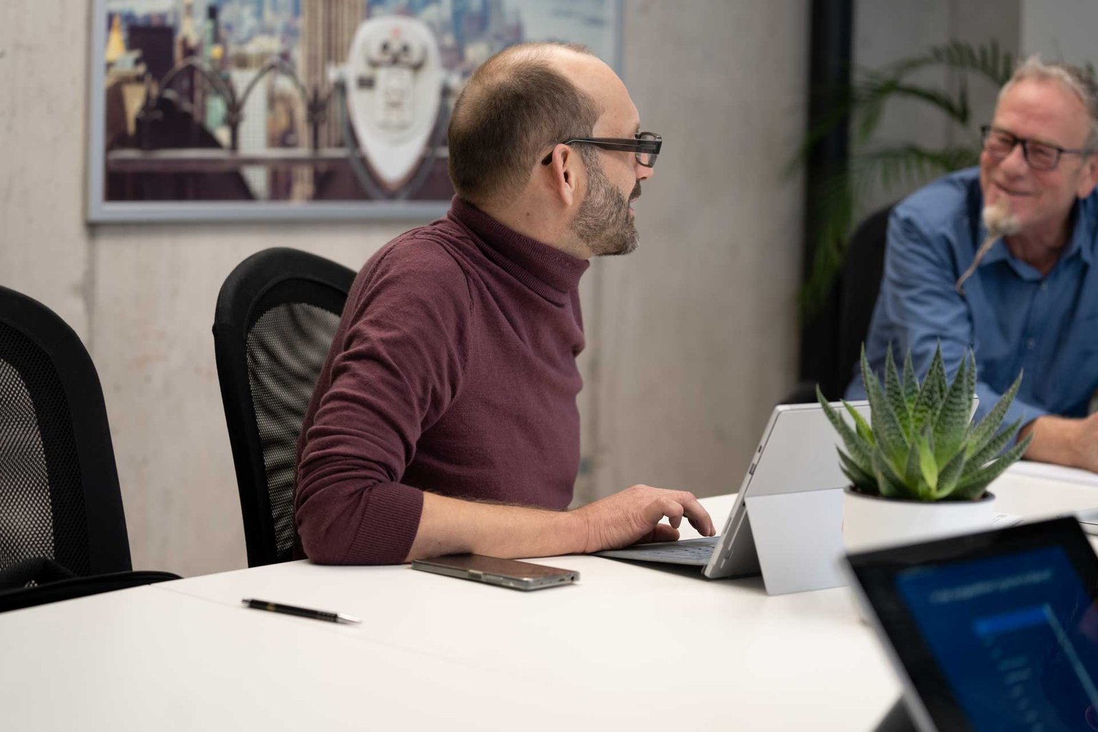 Ein Mann befindet sich in einem Meeting, arbeitet am Laptop und unterhält sich mit Kollegen über die neue Website